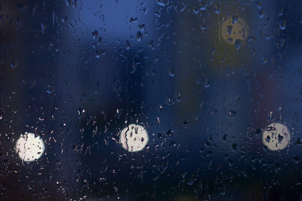 Raindrops on the glass and reflections of street lights in the background. Depression and thoughts